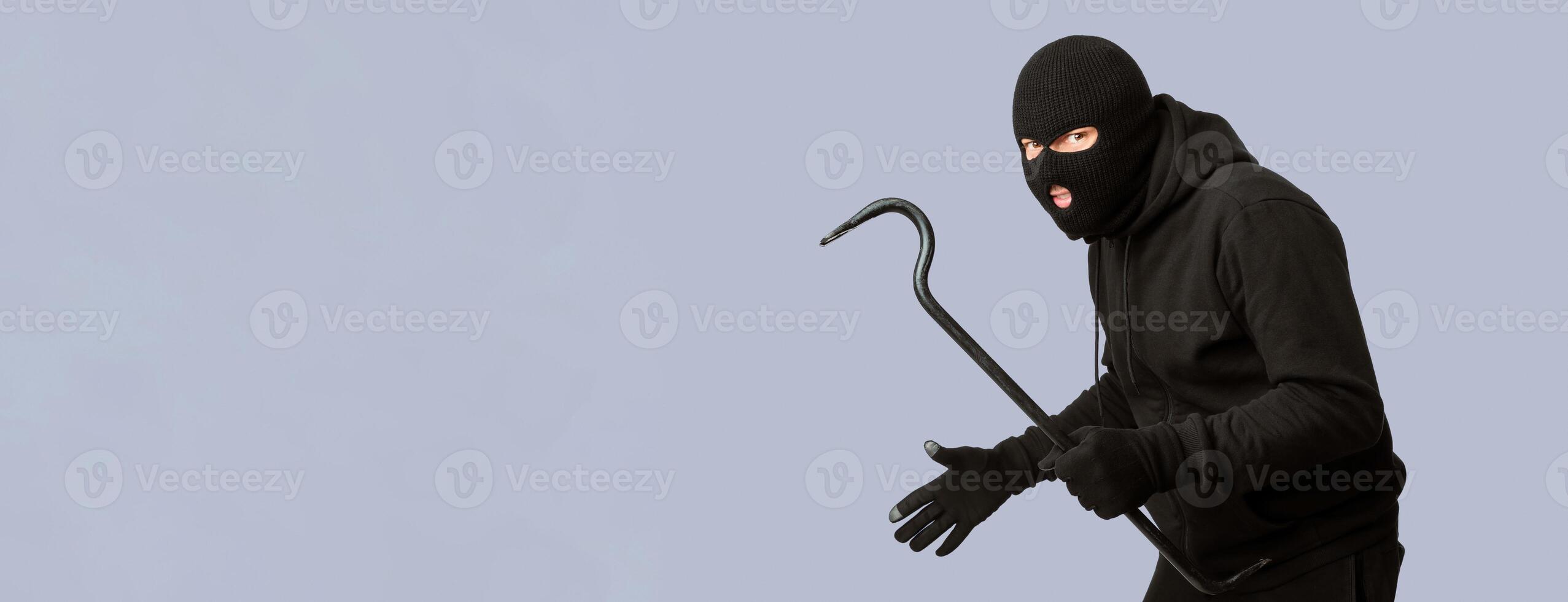 Cat Burglar Concept. Portrait of sneaky masked criminal holding crowbar, copy space, isolated over white studio wall photo