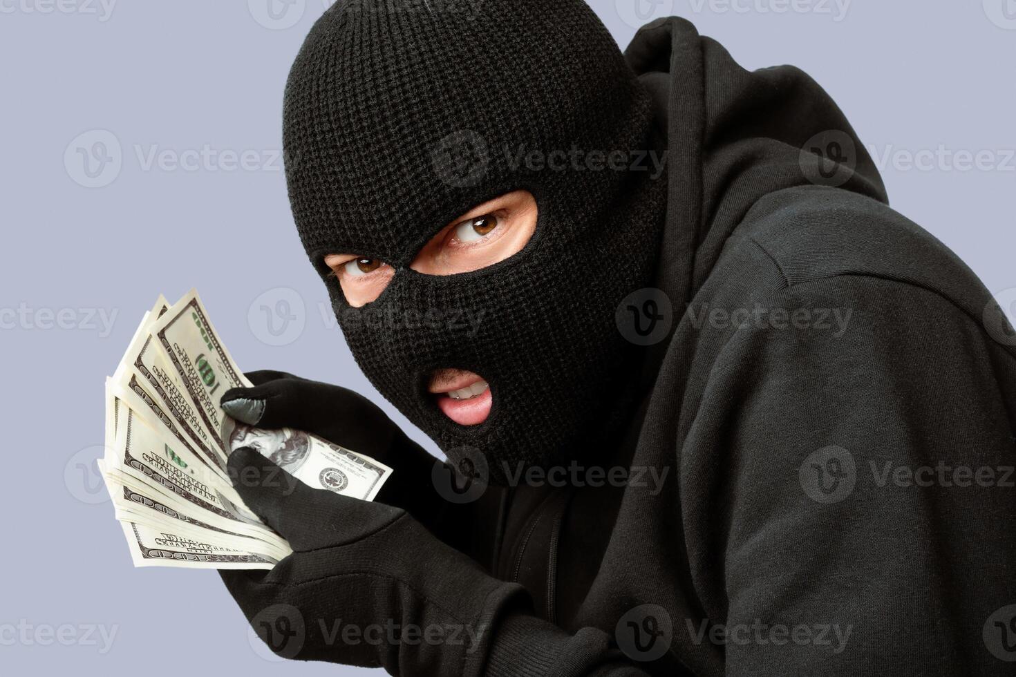 Closeup portrait of sneaky burglar with black mask and gloves counting money and looking at camera, isolated on white photo