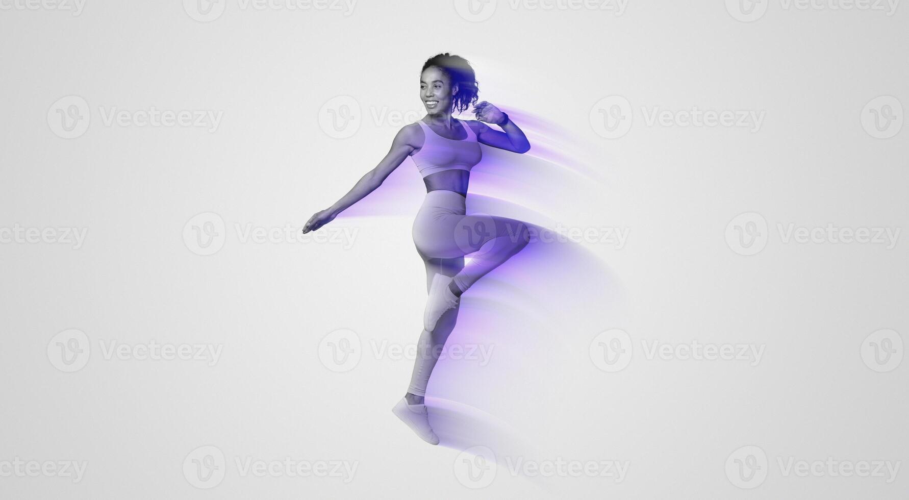 Young African American woman in yellow sportswear jumping doing knee to elbow exercise on blue studio backdrop, displaying athletic motivation during workout. Healthy sport training photo