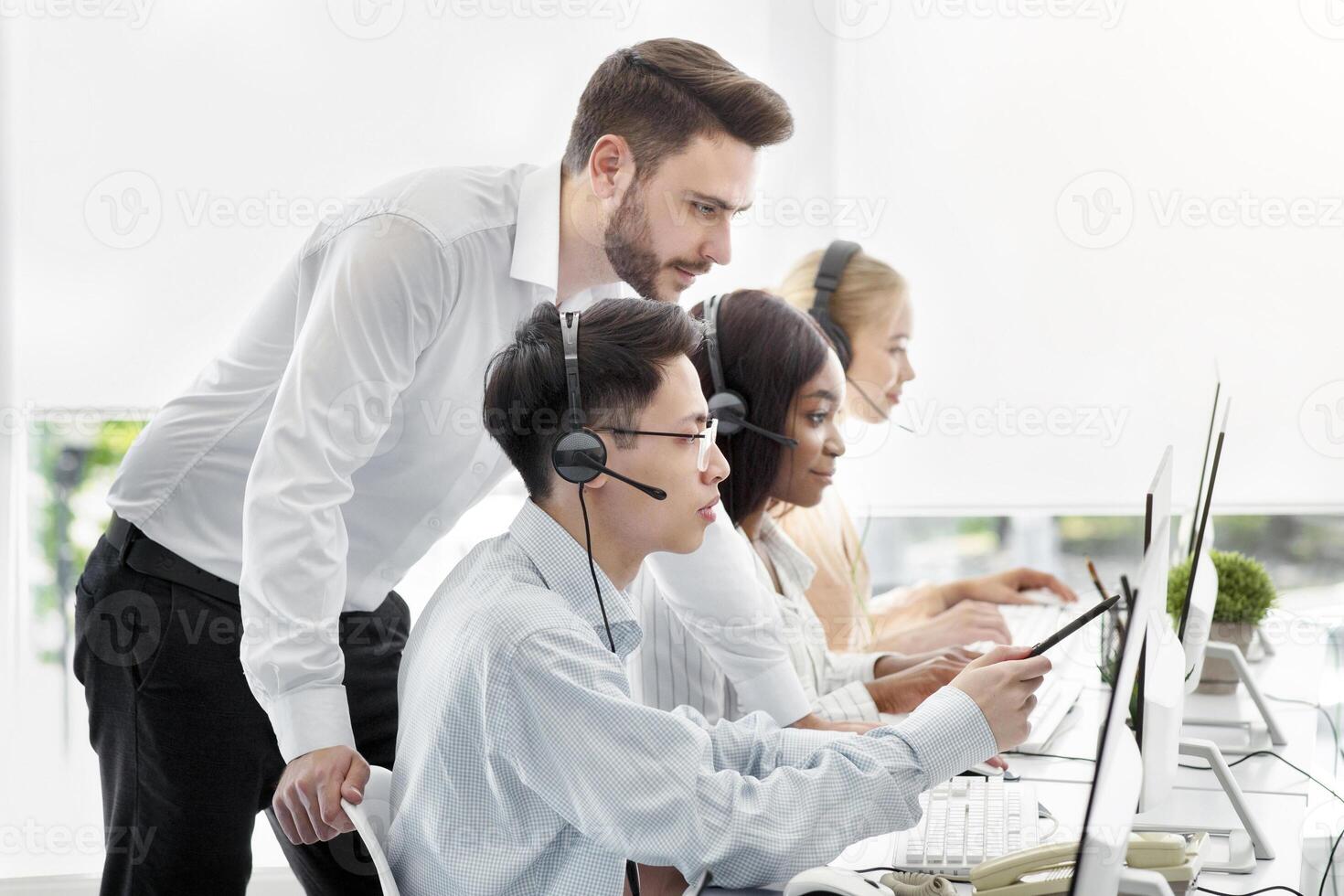 Customer service administrator helping his supervisee to execute client's request at call centre. Hotline colleagues working at problem together in contemporary open space office photo
