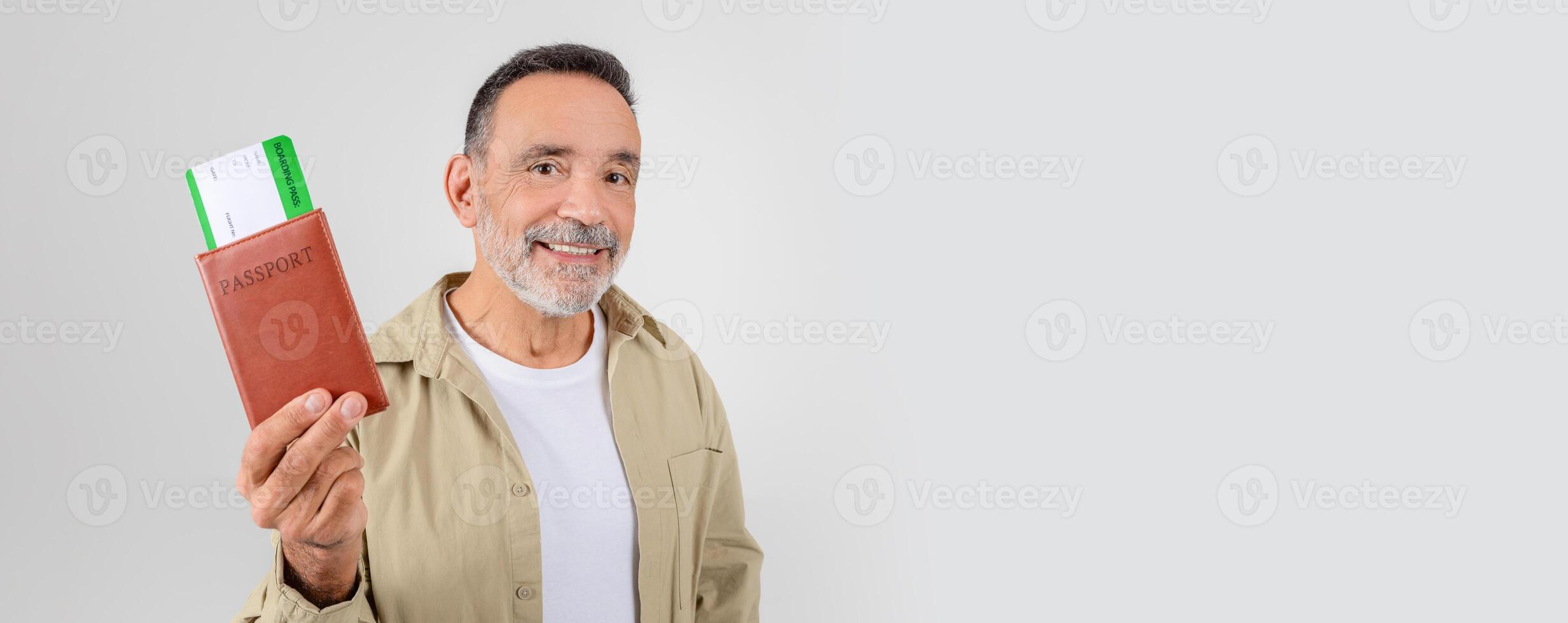 Smiling elderly gentleman displays a passport with flight tickets against a gray background, anticipating travel photo