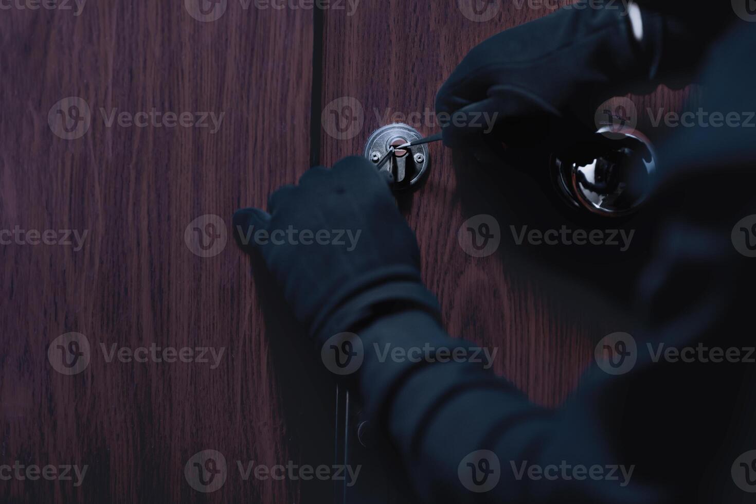 Closeup of unrecognizable robber cracking door lock with metal picklock tool during house breaking photo