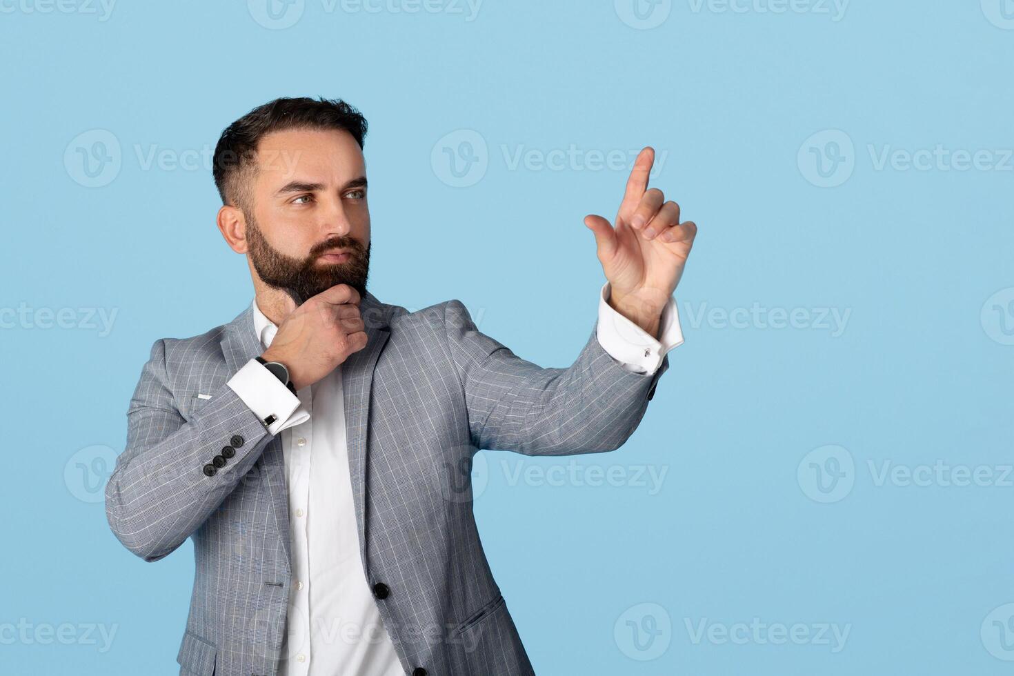 Corporate manager in formalwear selecting something on virtual screen over blue studio background, space for design. Millennial businessman choosing option on touchscreen, mockup photo