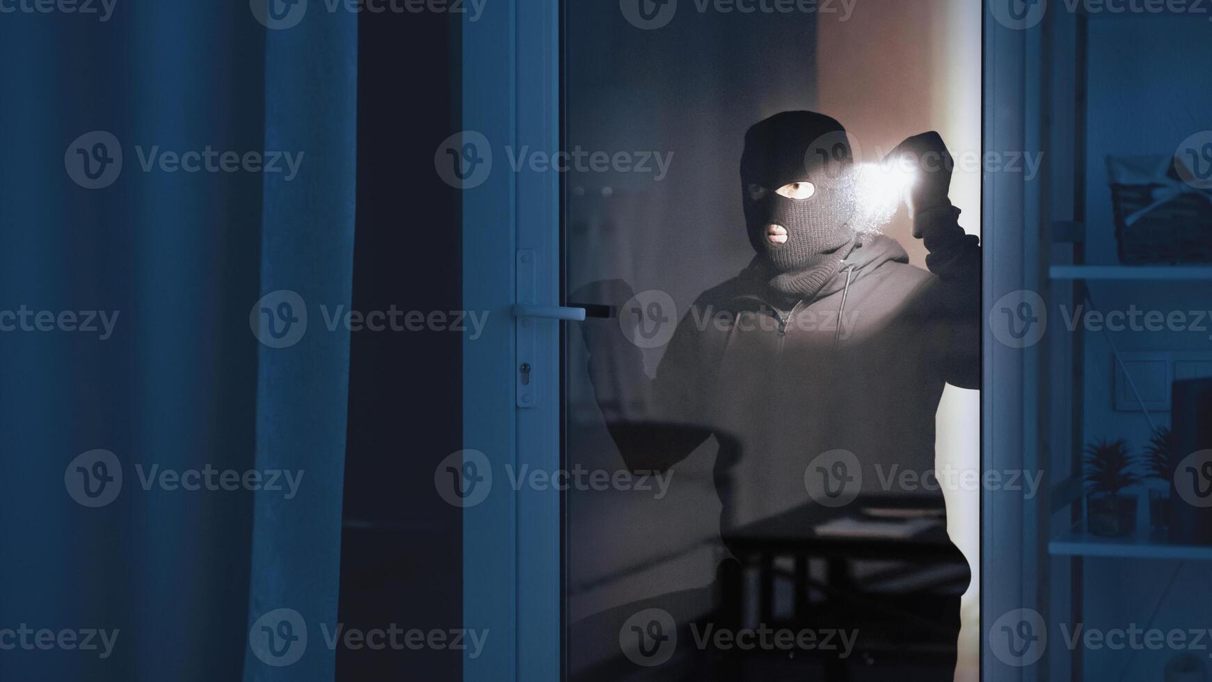 Criminal Act Concept. Portrait of robber checking apartment through balcony door, using flashlight torch, copy space photo