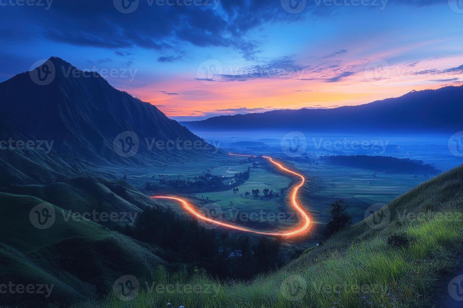 Winding road illuminated by lights at twilight in mountain valley photo