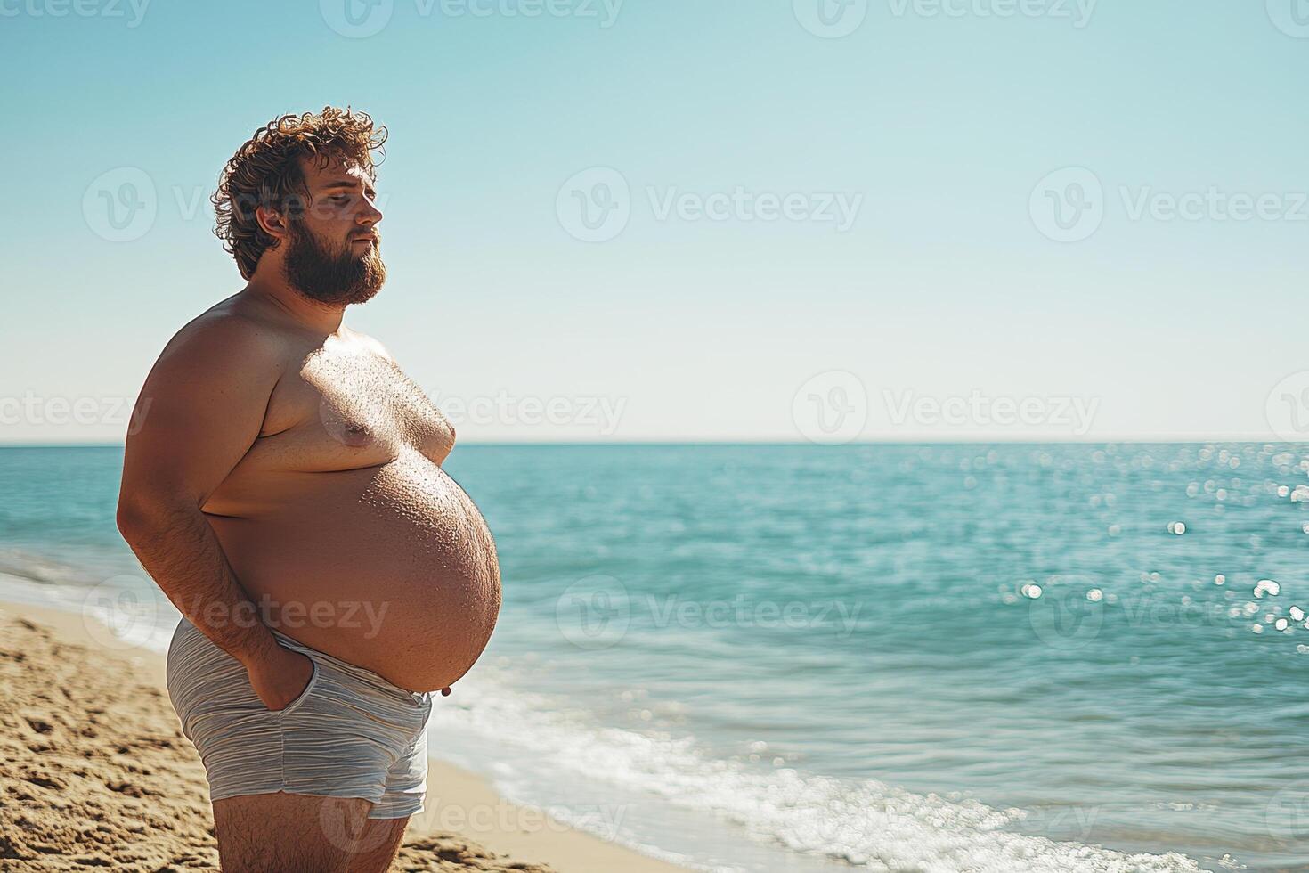Man with a belly standing on a beach under bright sun photo