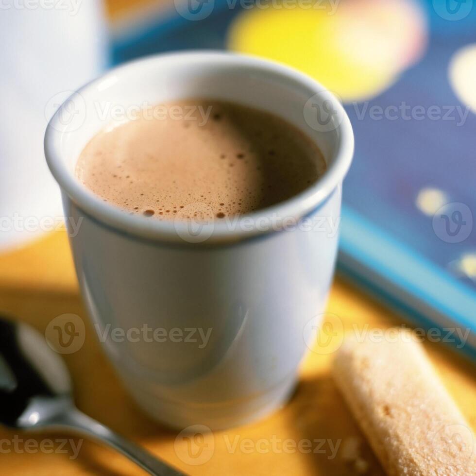 A cup of hot chocolate with a spoon and a book photo