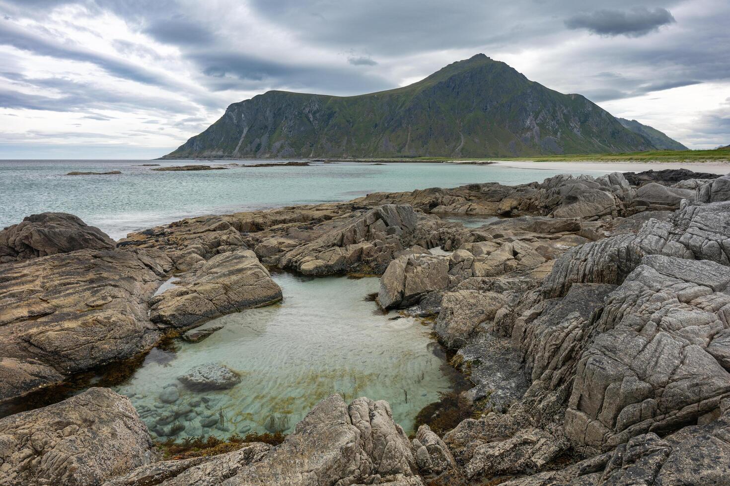 Sandy beach with stones and clear water pond and rocky mountains in cloudy background, Lofoten Norway photo