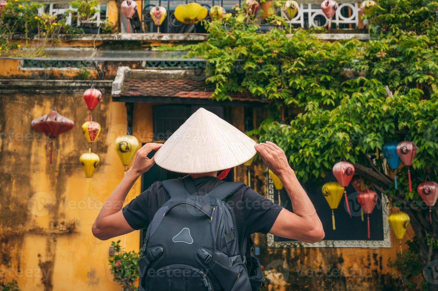 back of Asian male traveler tourist in traditional vietnamese hat on street in old town in Hoi An city in Vietnam in Asia photo