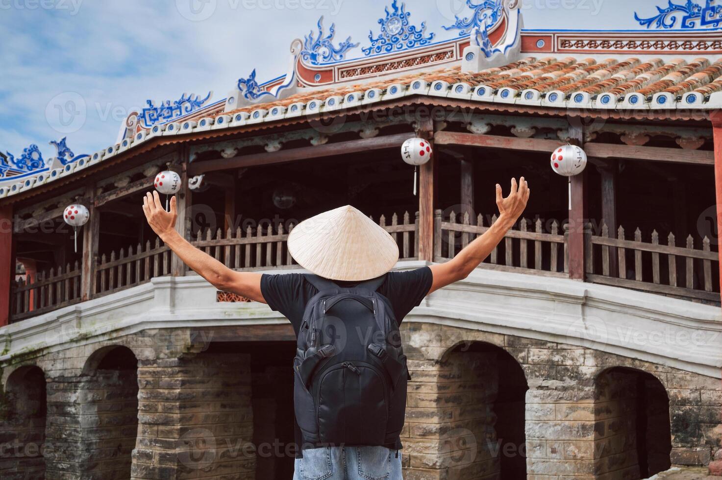 back of male traveler tourist in a Vietnamese hat at ancient Japanese covered bridge in old town in Hoi An in Vietnam in Asia photo