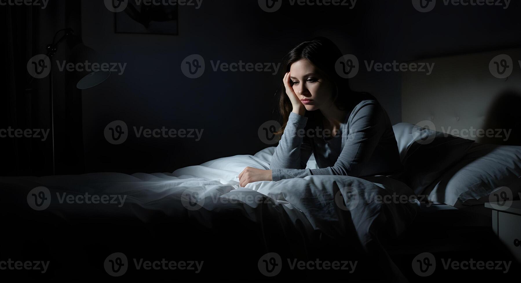 A woman sitting in bed at night with her head on her hand photo