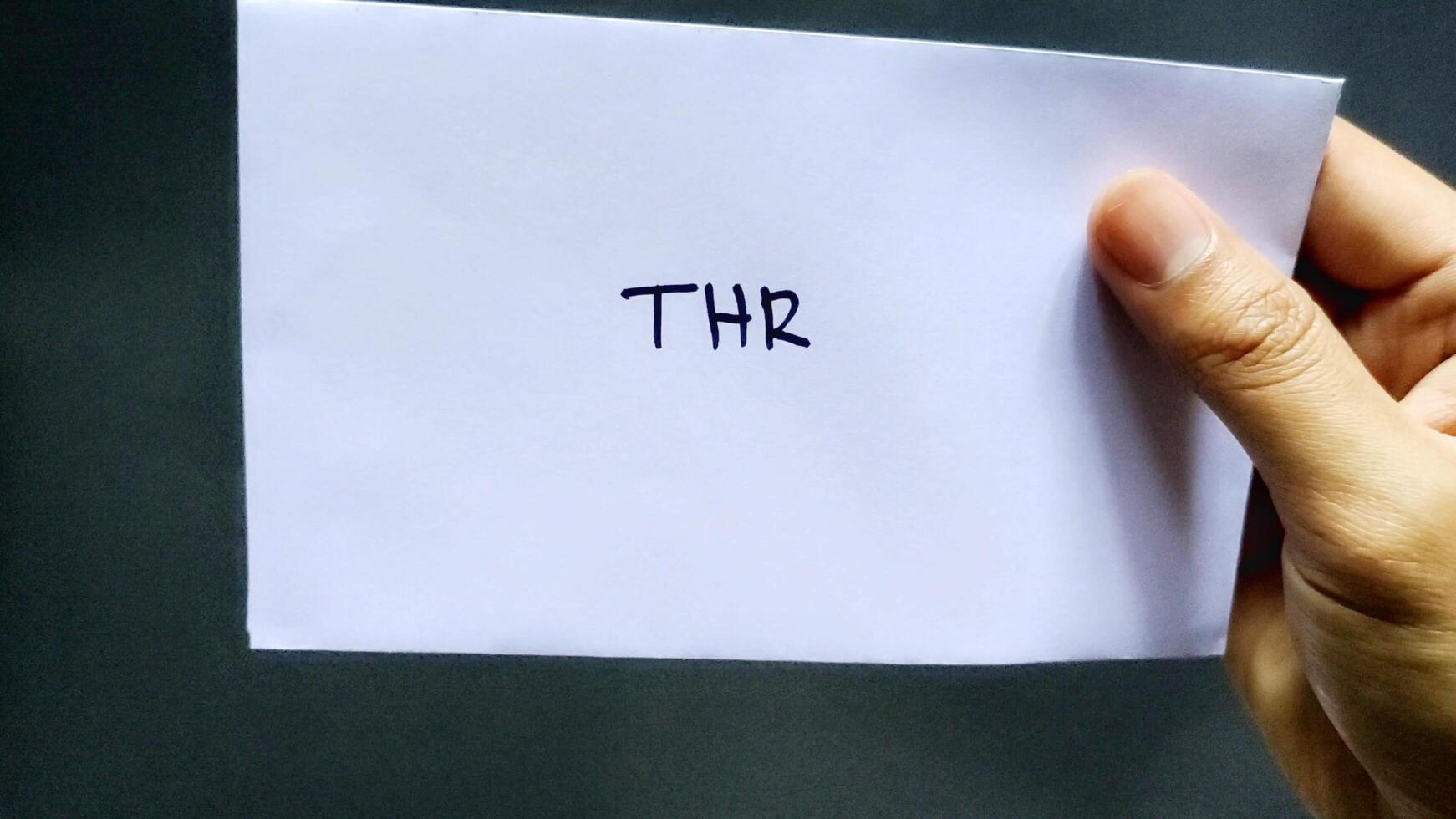 This man holding a white envelope that says THR. This envelope contains one month's salary allowance which is usually given to employees before the Islamic holidays photo