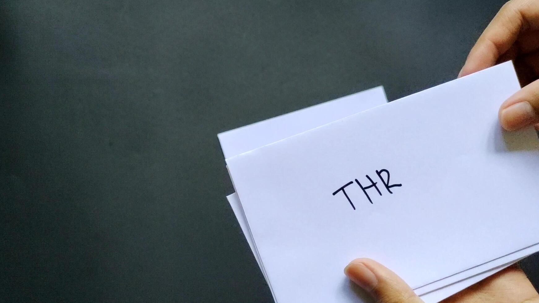 Woman hand holding a white envelope labeled THR, isolated on black background. Negative space photo