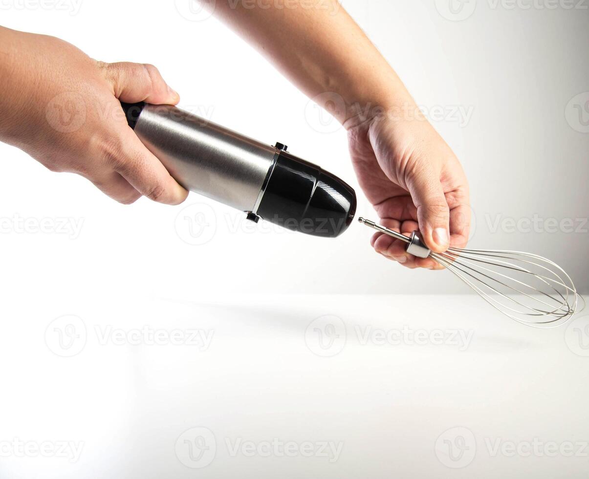 Modern immersion blender with whisk in hand on white background, close-up photo