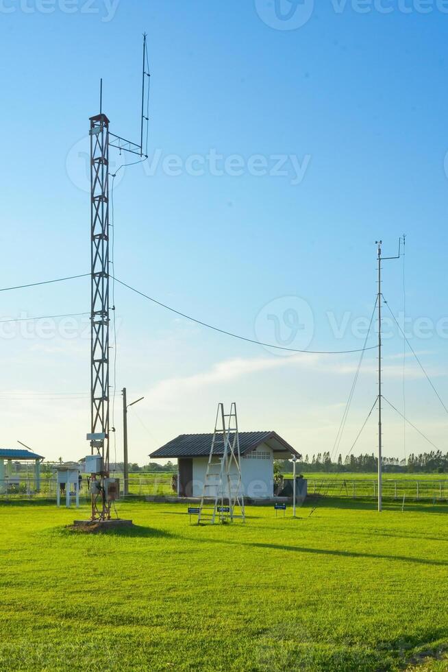 Weather monitoring station with tower and shelter in open field under clear sky photo