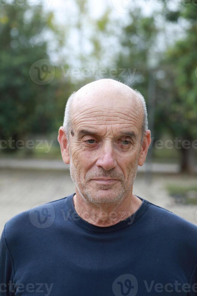 Bald Senior Man Smiles Slightly In The Nature Among The Trees photo