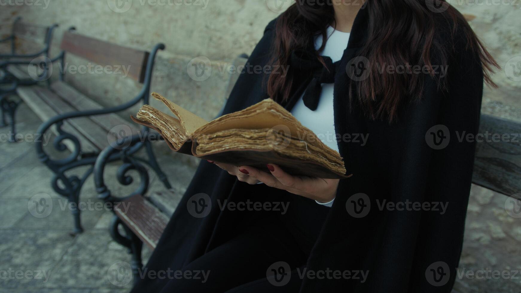 Woman With Cloak Reads The Mysteries In The Book Sitting On A Bench In The City photo