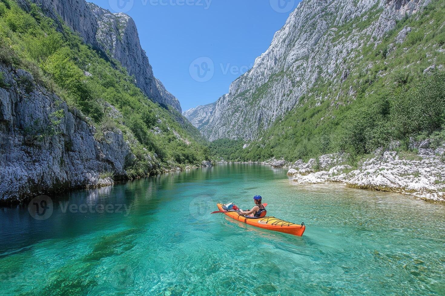 Person kayaking in crystal clear turquoise river amidst towering cliffs under a clear sky. photo