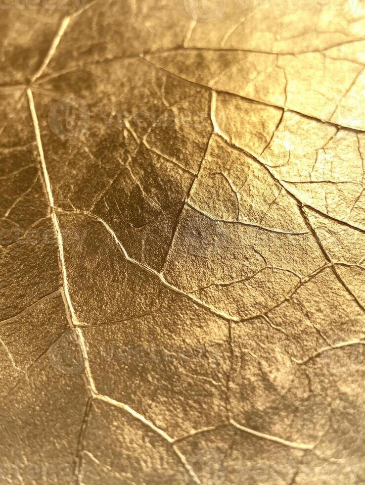 Close-up of a cracked golden texture resembling a leaf pattern, shining under warm light. photo