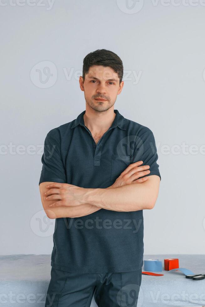 With arms crossed. Professional physiotherapist is standing indoors with kinesio tape photo