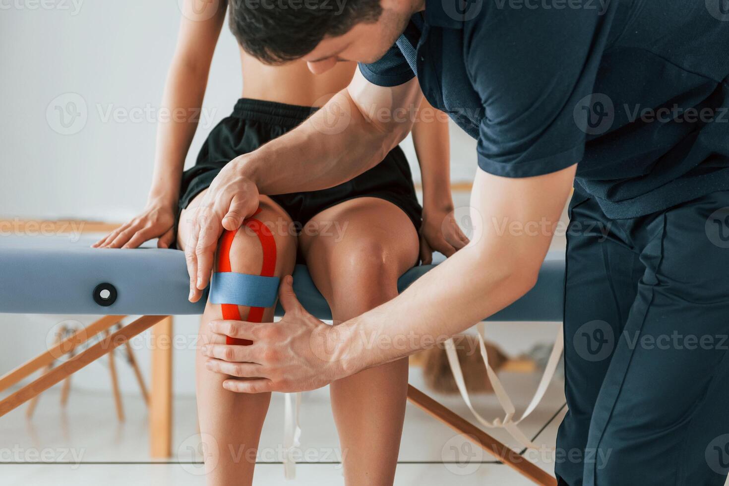 Working with a legs. Woman visiting physiologist that putting kinesio tape on the skin photo