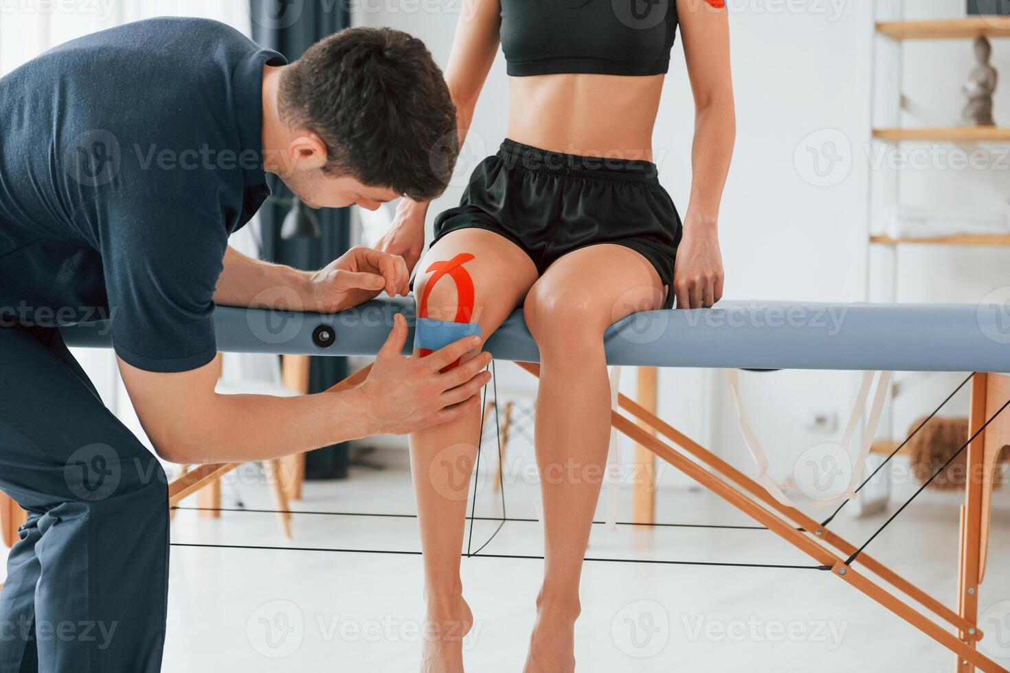 Working with legs. Woman visiting physiologist that putting kinesio tape on the skin photo