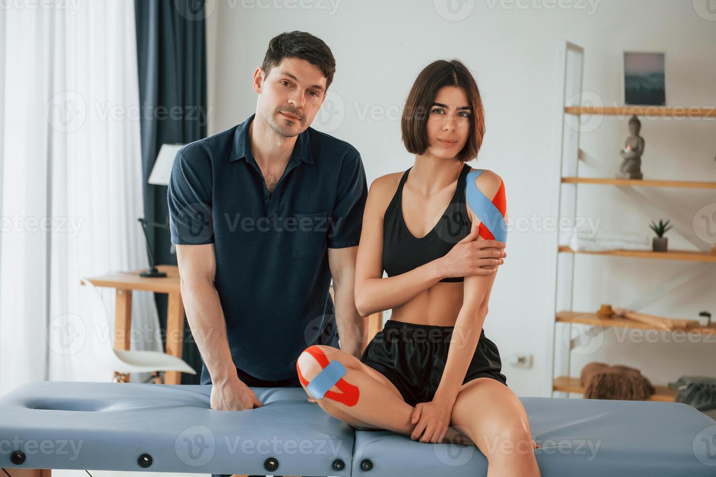 Looking at the camera,.. Woman visiting physiologist that putting kinesio tape on the skin photo