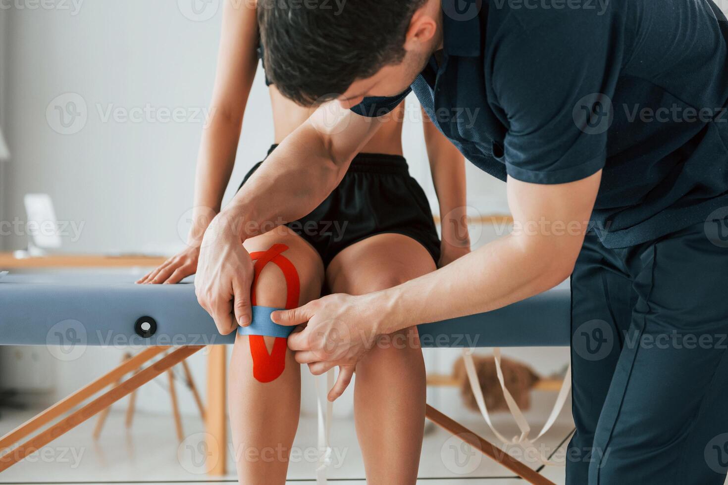 Working with legs. Woman visiting physiologist that putting kinesio tape on the skin,. photo