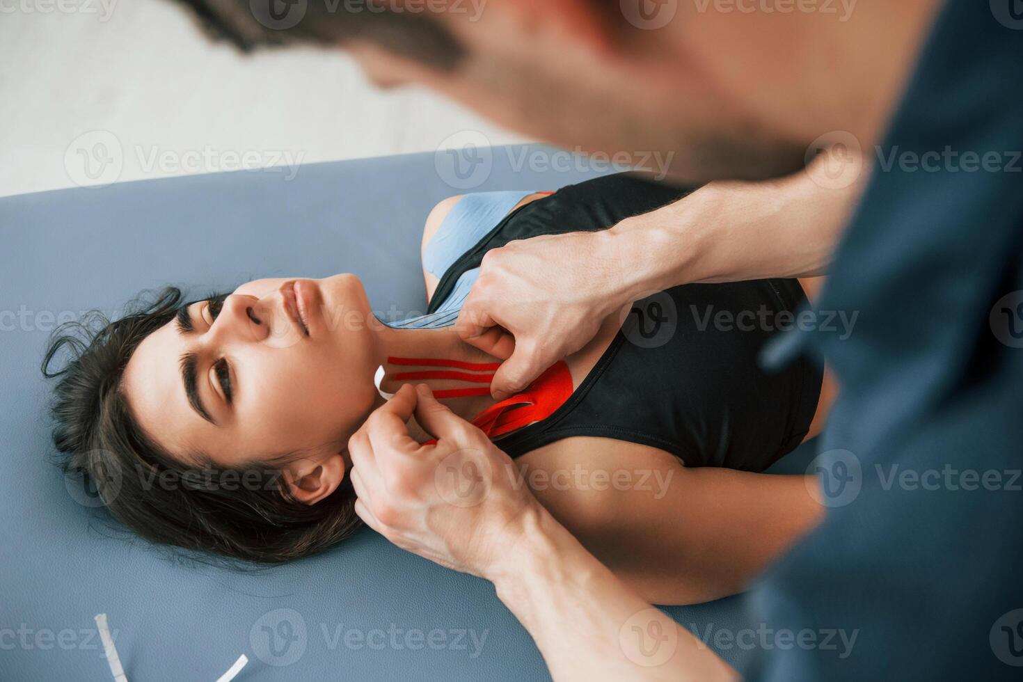 Laying down on the table,. Woman visiting physiologist that putting kinesio tape on the skin photo