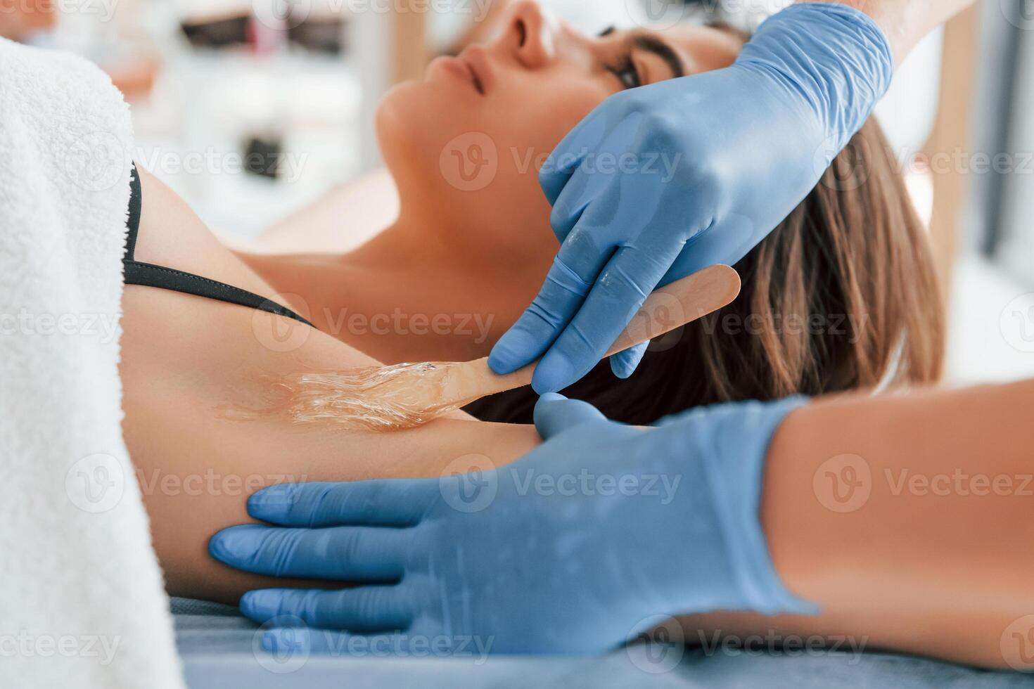 Putting cream on the armpits. Woman is having, sugaring procedure in the clinic by female doctor photo