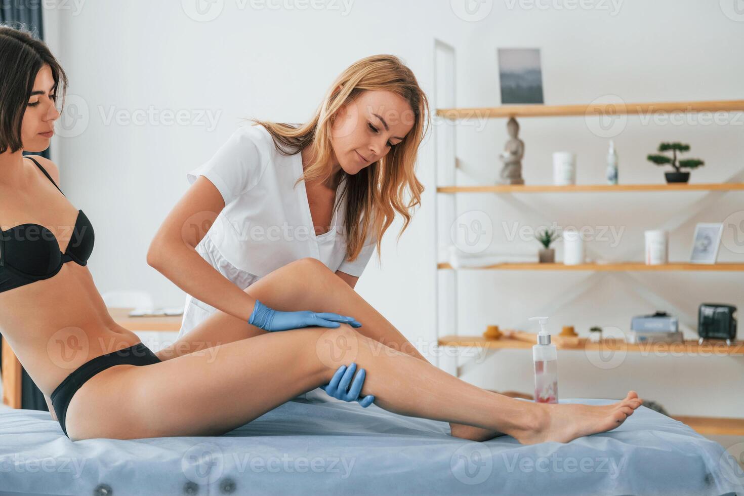 Putting cream on the legs. Woman is having sugaring procedure in the clinic by a female doctor photo