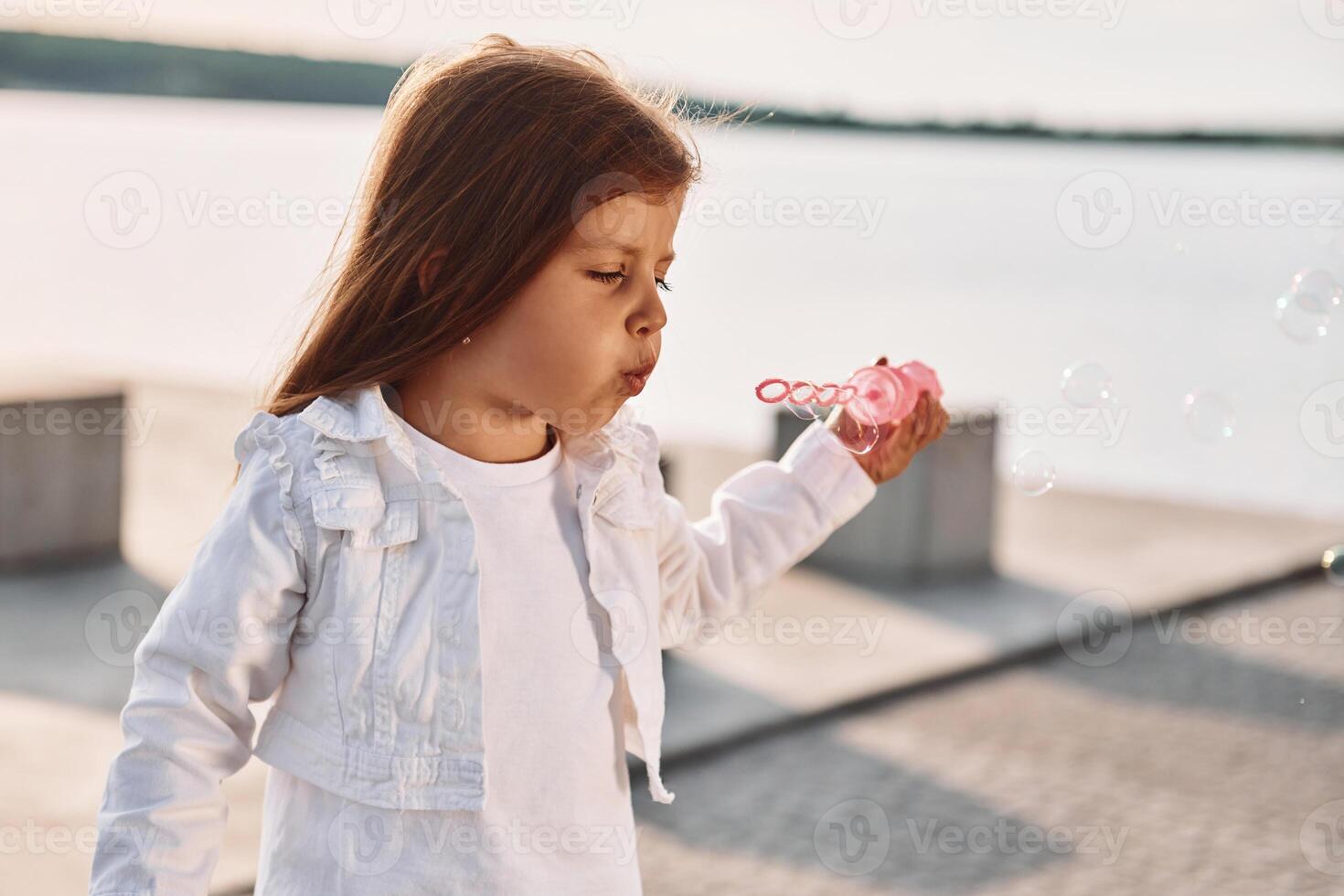 Playing with bubbles, ,Little cute girl having fun outdoors at summer near the lake photo