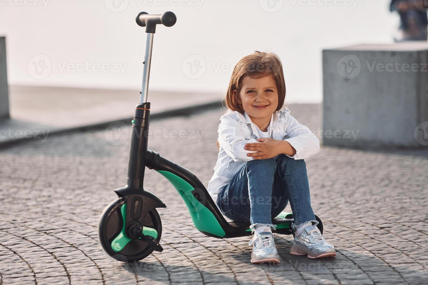 Cute little girl with scooter is outdoors in summertime photo