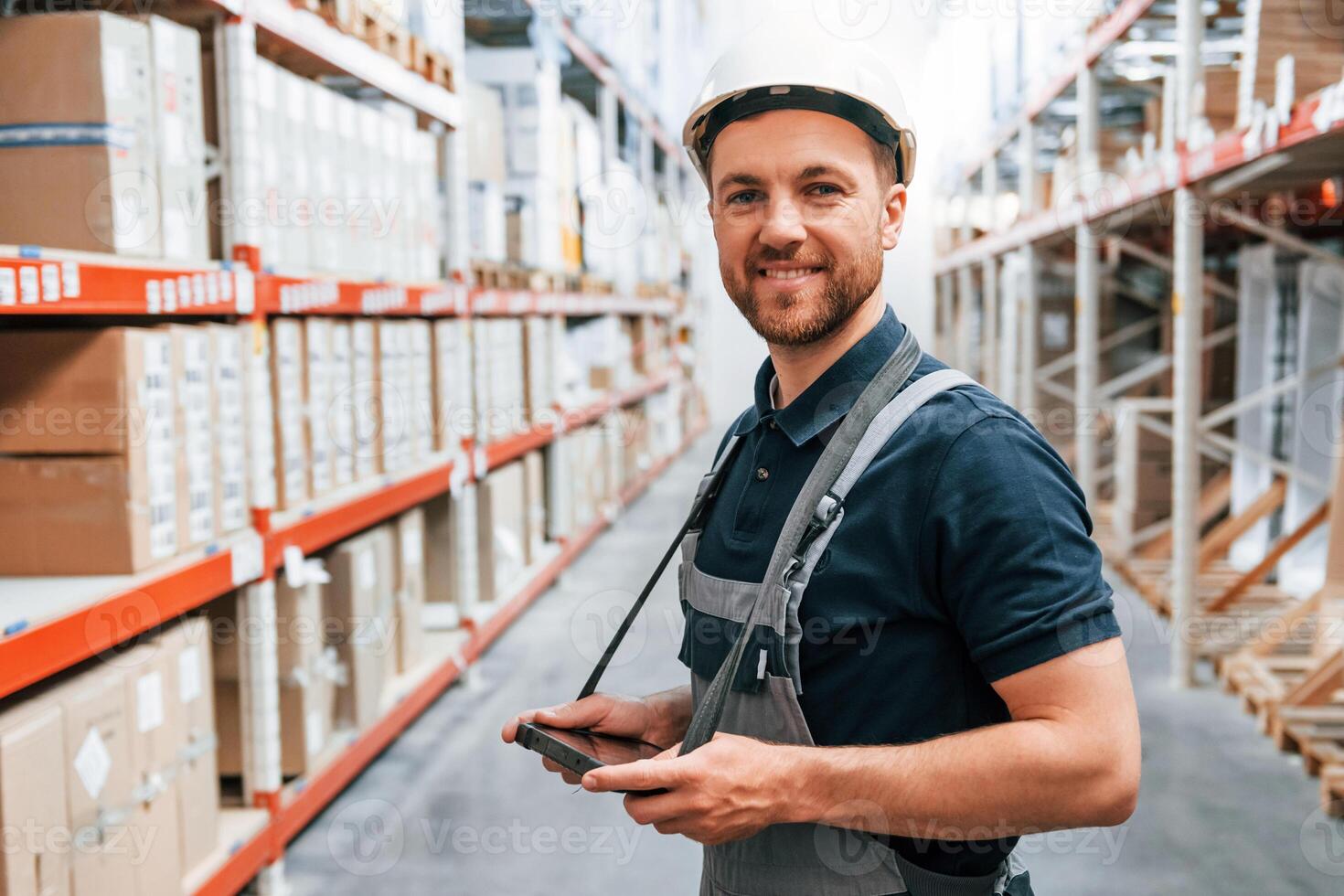 Side view of man that holding tablet. Employee in uniform is working in the storage at daytime photo