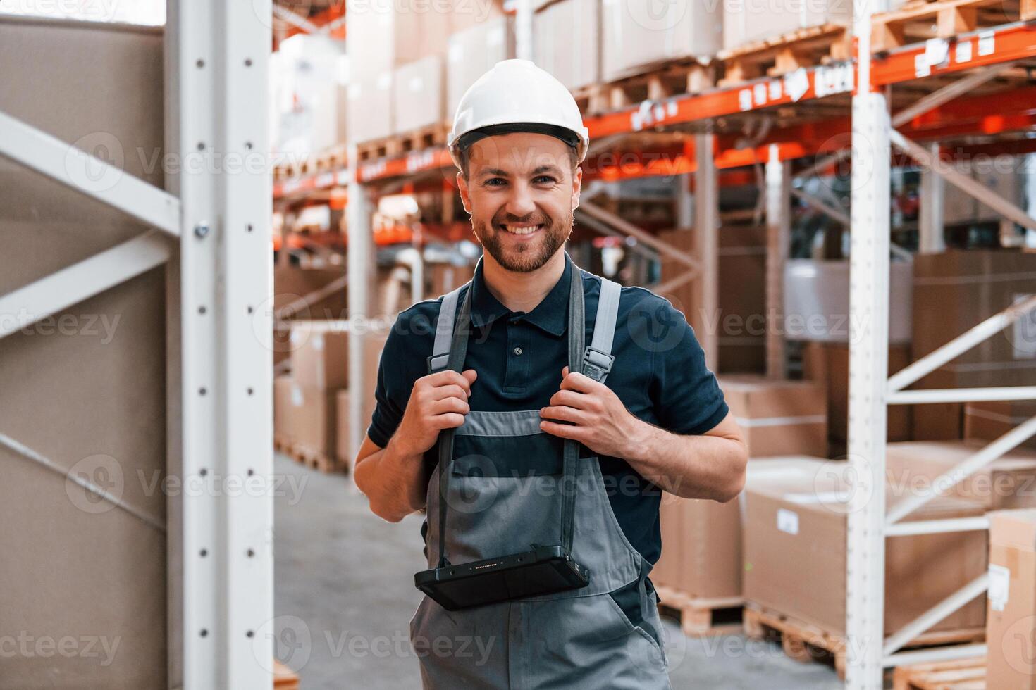 Smiling for the camera. Employee in uniform is working in the storage at daytime,, photo