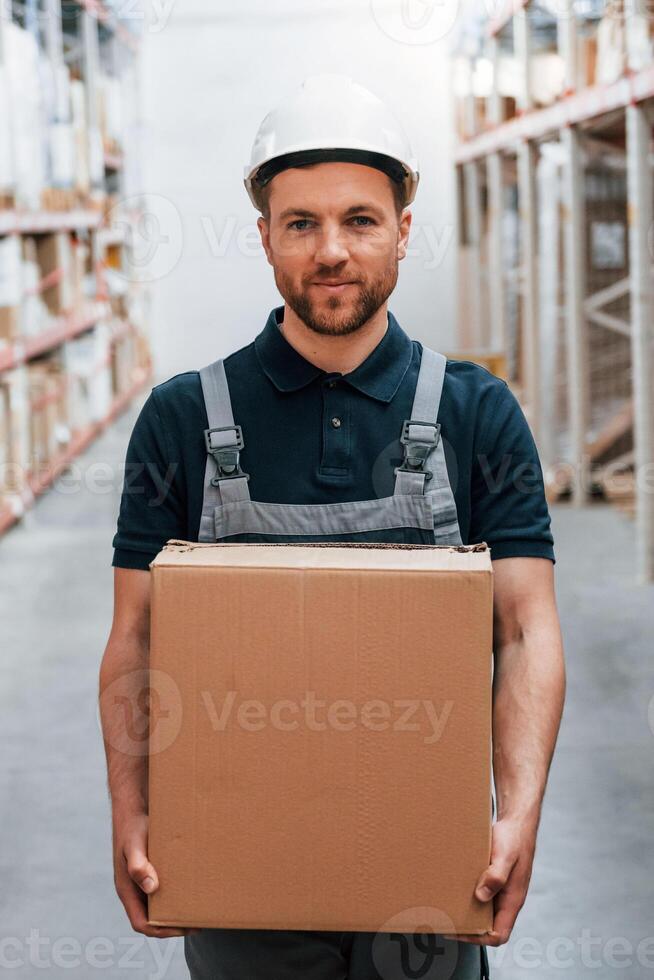 With delivery package in hands. Employee in uniform is working in the storage at daytime photo