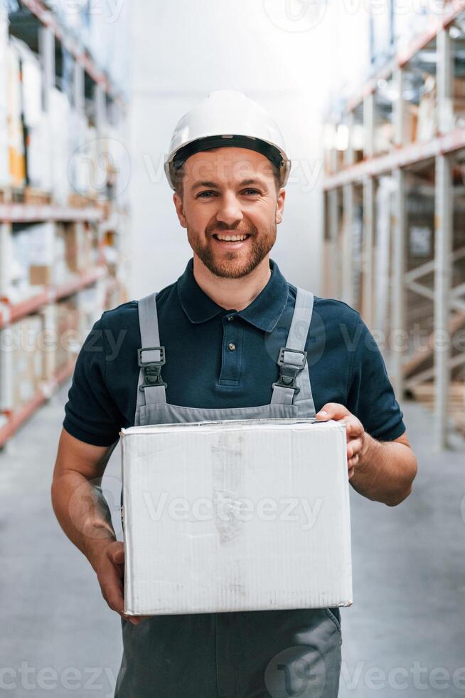 Holding white box and smiling, Employee in uniform is working in the storage at daytime,, photo