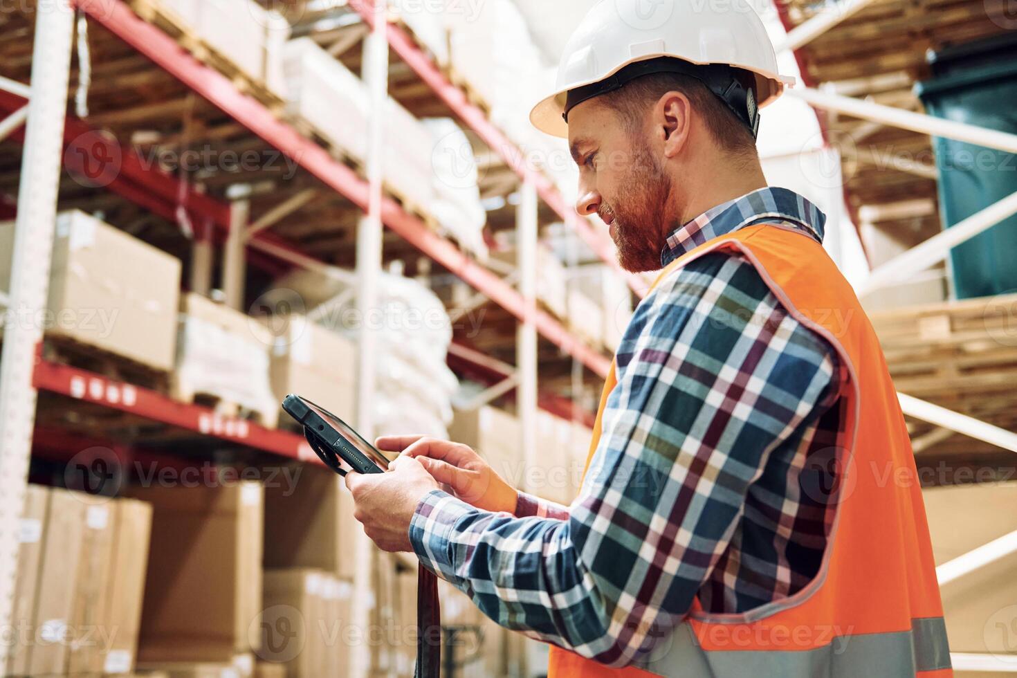 Holding tablet in hands. Employee in uniform is working in the storage at daytime, photo