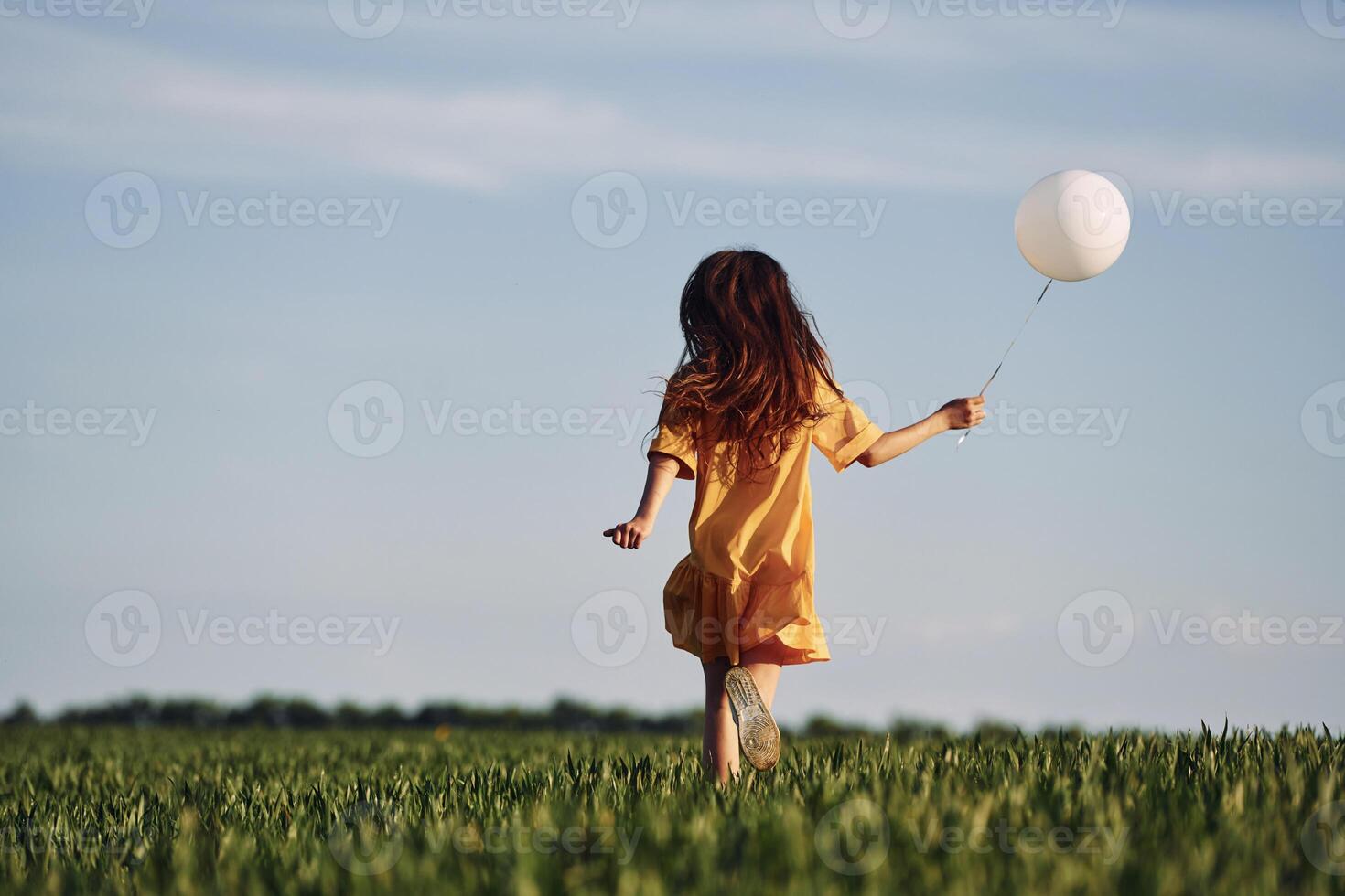 Running with balloon in hand. Happy girl have a walk outdoors on the field at summer photo