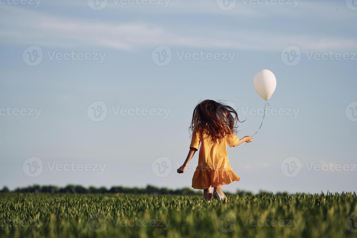 Running with balloon in hand. Happy girl have a walk outdoors on the field at summer., photo
