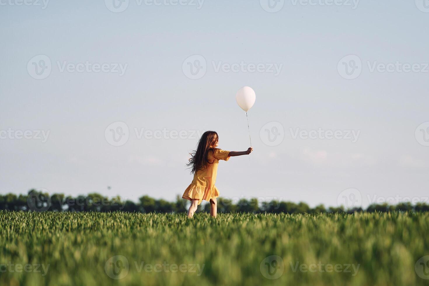 Playing with balloon. Happy girl have a walk outdoors on the field at summer photo