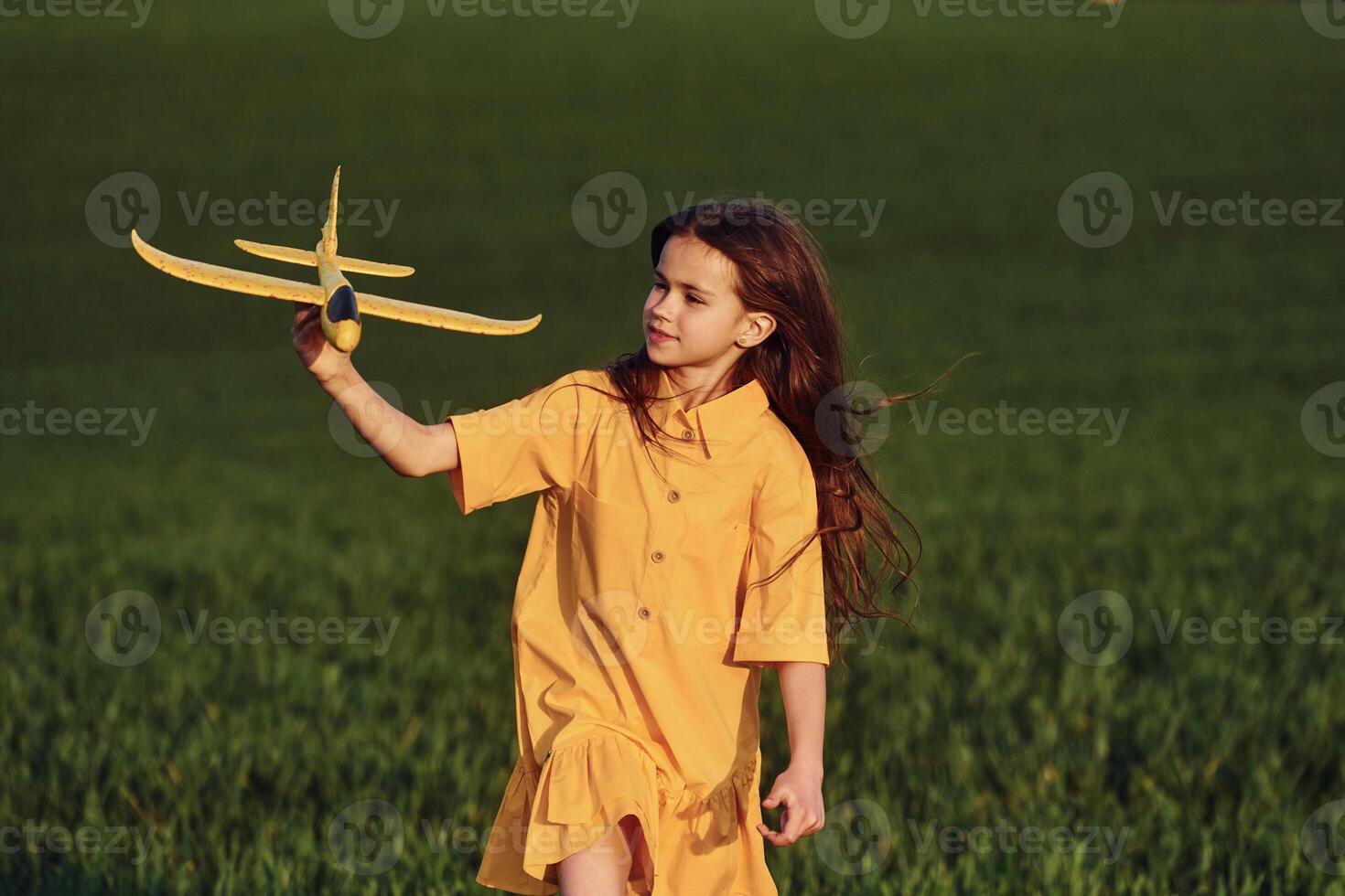 Running forward with toy plane. Happy girl have a walk outdoors on the field at summer photo