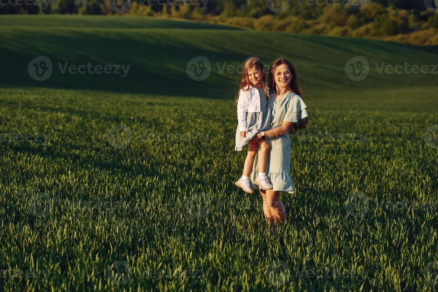 Standing and posing for a camera. Mother and daughter have fun outdoors on the field at summer. photo