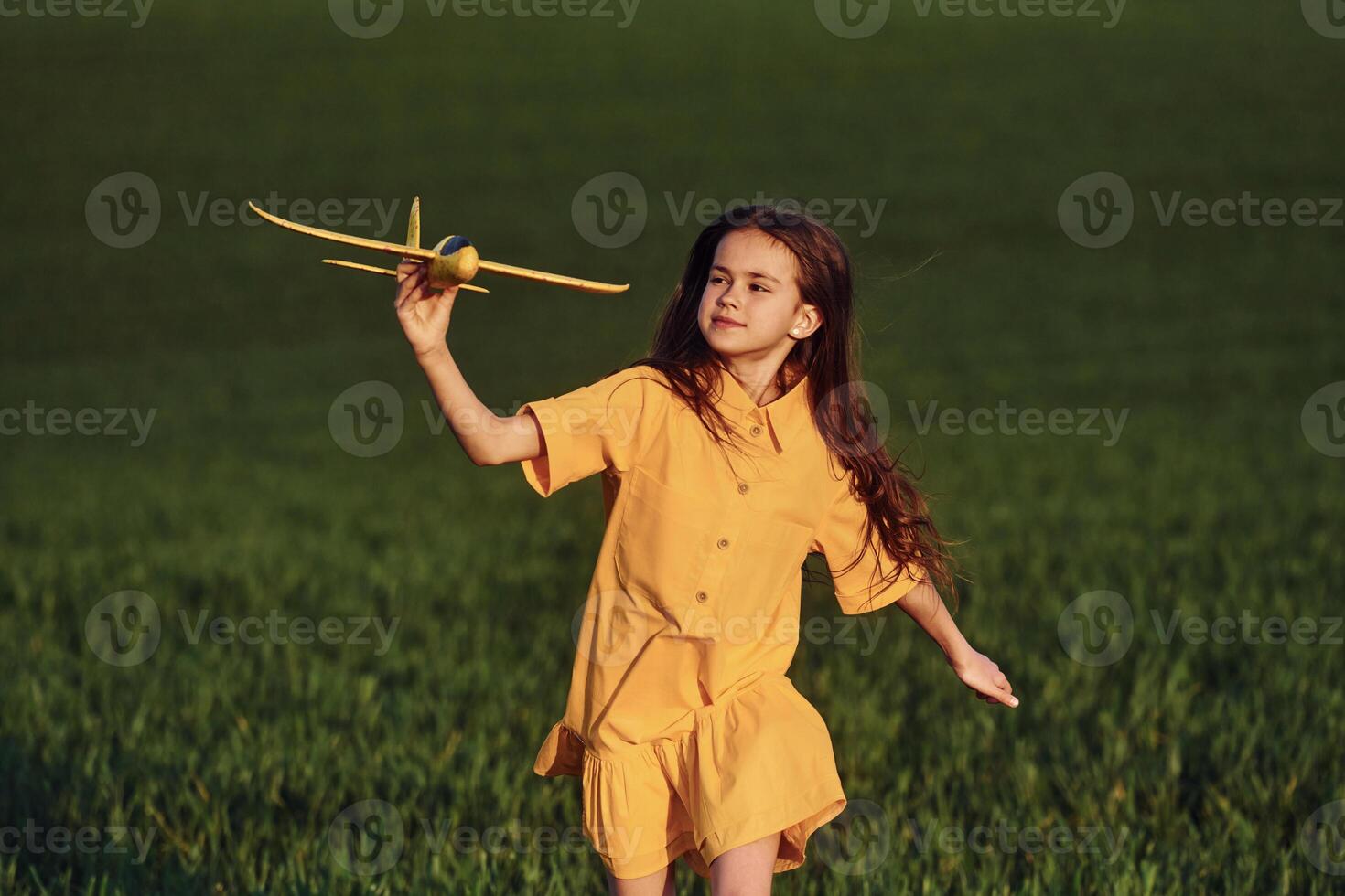 Running forward with toy plane. Happy girl have a walk outdoors on the field at summer., photo