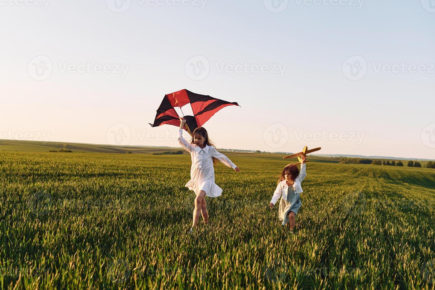 Two girls have fun outdoors on the field at summer with red kite in hand photo
