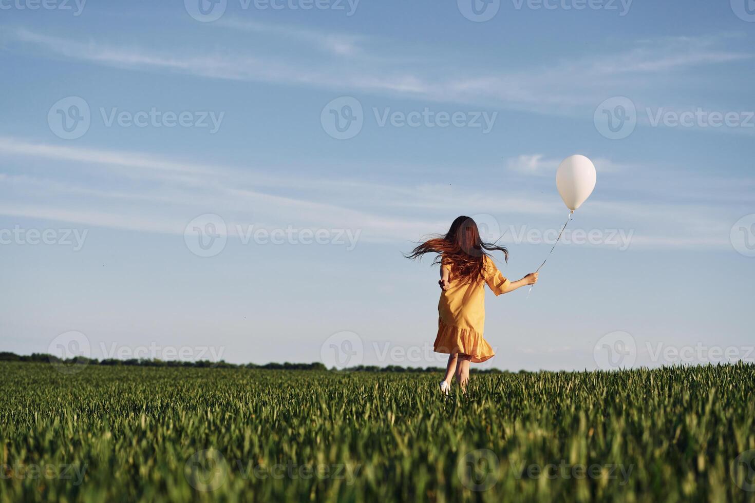 Running with balloon in hand. Happy girl have a walk outdoors on the field at summer. photo