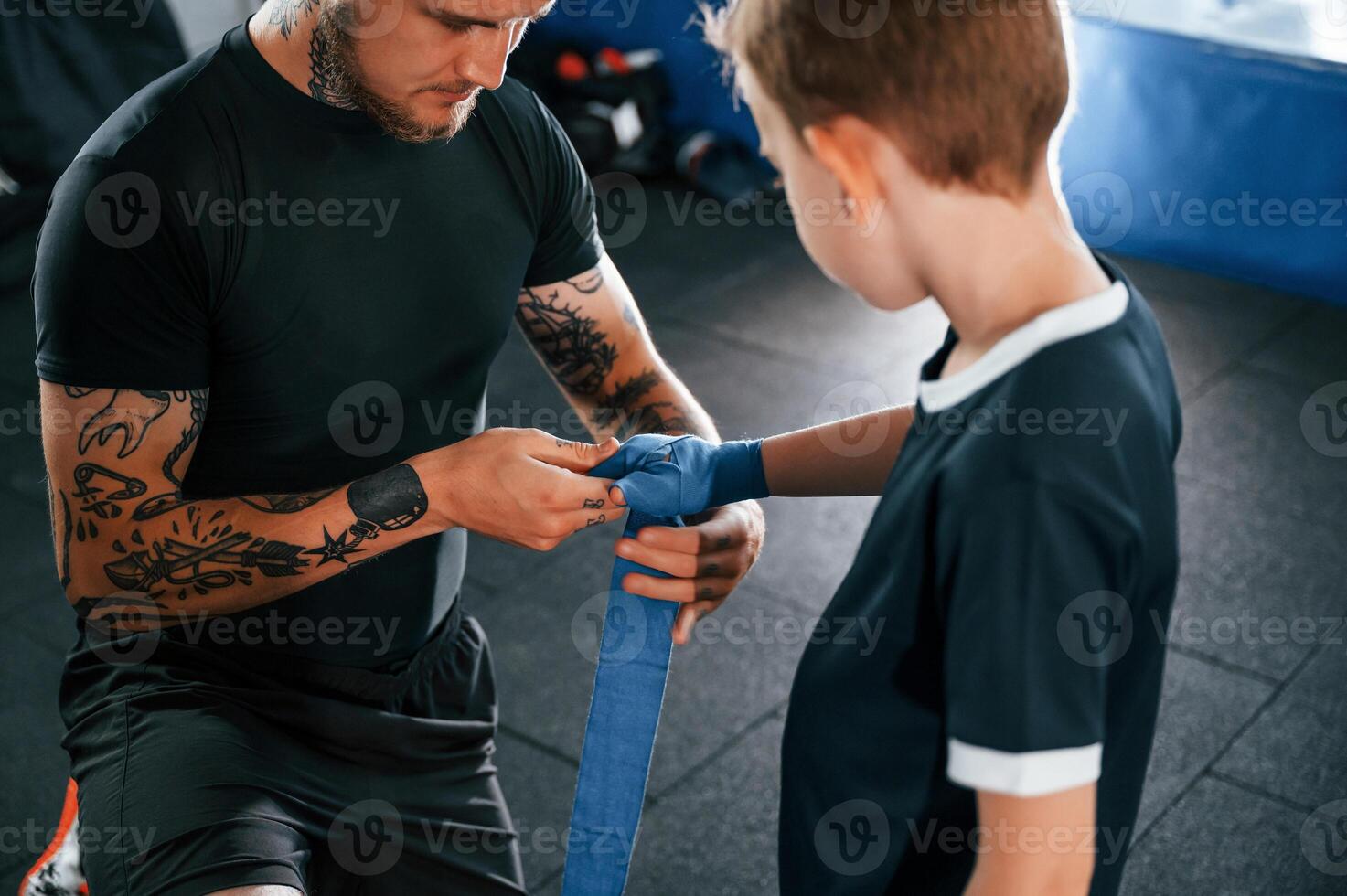 Wearing the boxing hand wraps. Coach is with boy in the practice space, photo
