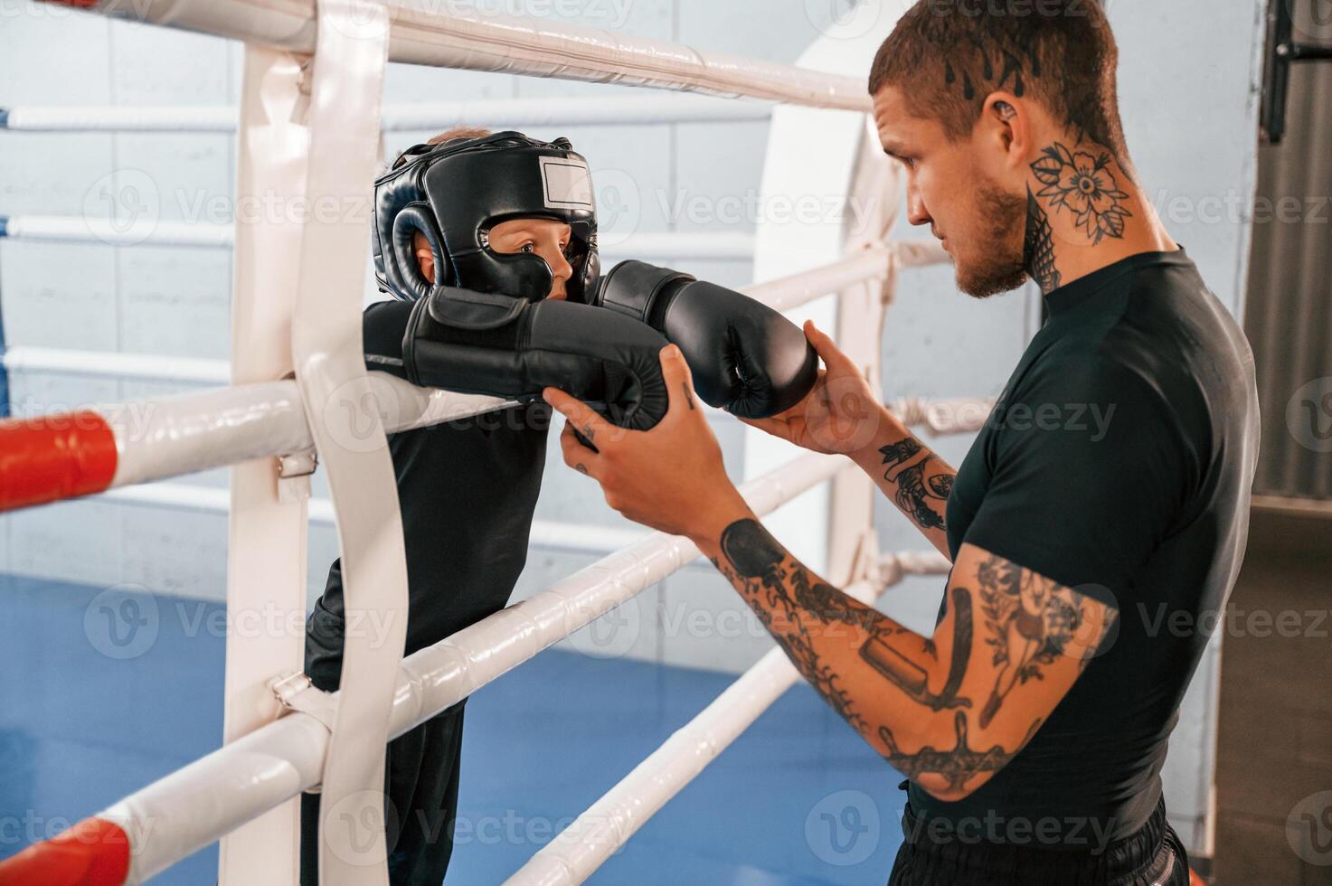 In protective helmet and with glowes. On the ring. Coach is teaching the boy box techniques indoors,. photo