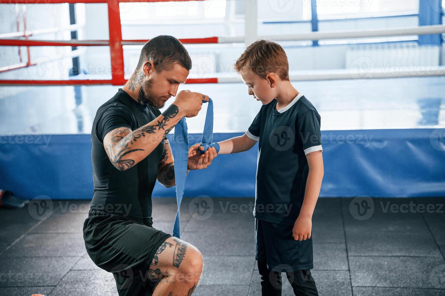 Wearing the boxing hand wraps. Coach is with boy in the practice space., photo