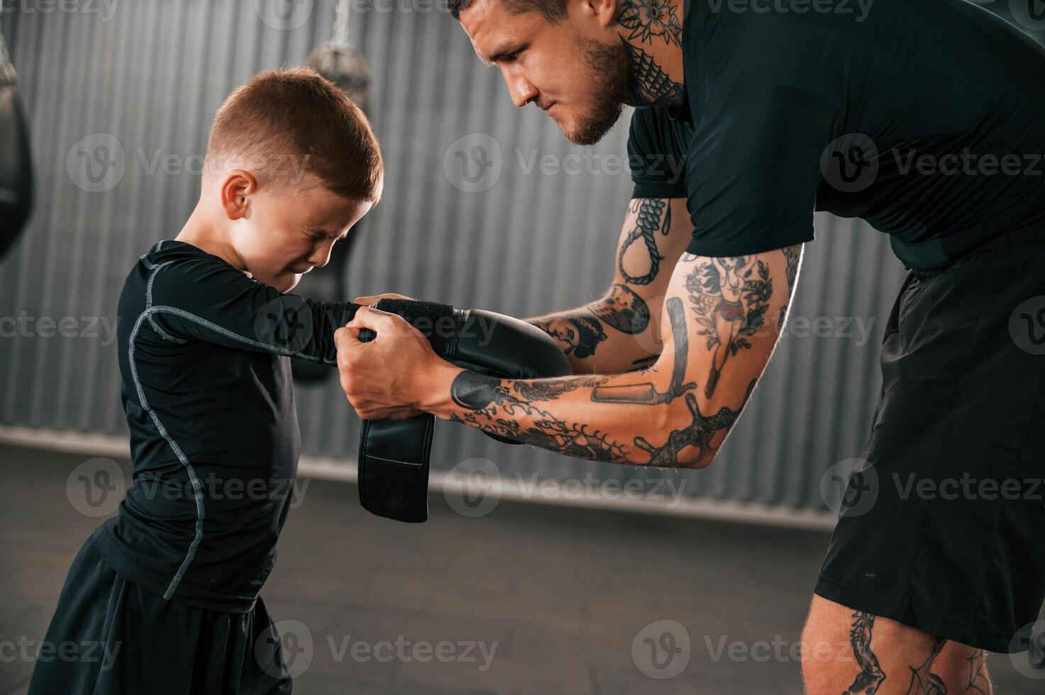Man is helping child to wear the glowes.. Coach is teaching the boy box techniques indoors photo